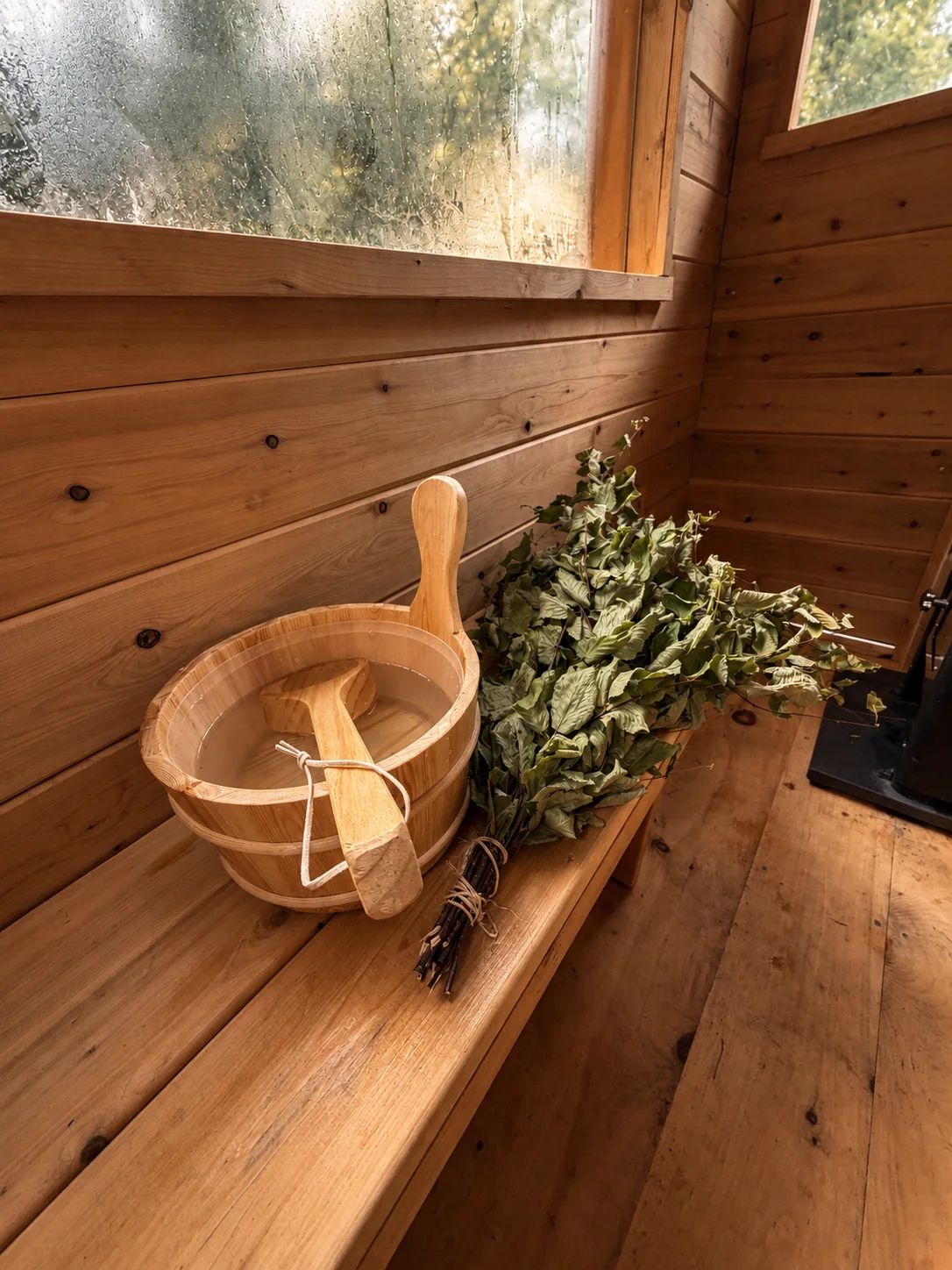 Wooden water bucket and leafy venik waiting on a sauna bench