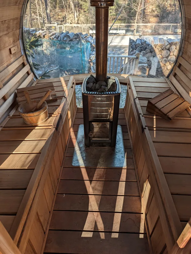 Finished sauna with wooden benches and a stove facing panoramic glazing